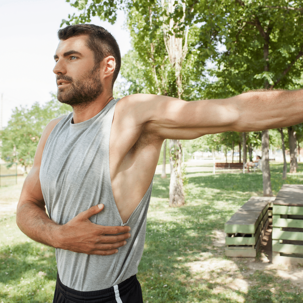 A man stretching in shoulder in a park.